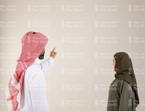 صورة من الخلف لرجل سعودي يرتدي الزي السعودي التقليدي يشير بإصبعه السبابة نحو الأمام أثناء حديثه مع امرأة سعودية ترتدي العباءة