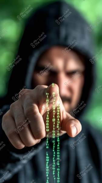 صورة لرجل يرتدي بدلة سوداء بأكمام طويلة وغطاء رأس. يشير بإصبعه نحو الكاميرا, مع تأثير رقمي على شكل أرقام ثنائية خضراء تظهر من إصبعه, مما يعكس موضوع التكنولوجيا أو الاختراق. الخلفية ضبابية مع درجات لون أخضر.