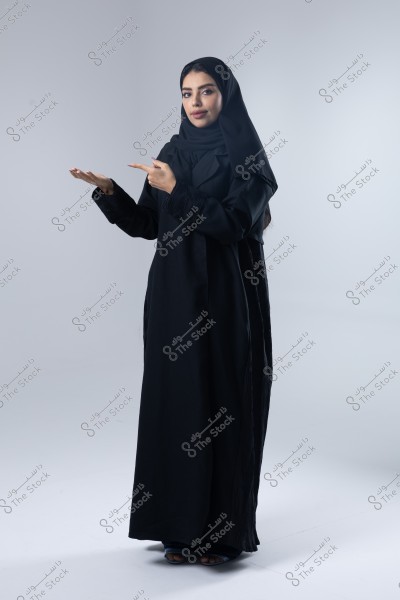 صورة لامرأة ترتدي عباءة سوداء وحجابًا, واقفة في وضع يدلي إلى جانبها في استوديو ذي خلفية بيضاء. يبدو أنها تنتمي إلى بيئة خليجية.\r\n\r\n-