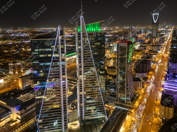 Aerial night view of Riyadh, Saudi Arabia, showcasing towering skyscrapers and illuminated roads. The iconic Kingdom Tower is visible in the background, with bright city lights stretching across the horizon.