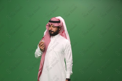 شاب سعودي على خلفية خضراء يرتدي الثوب و الشماغ، يقوم بعمل حركات بيده، يشرب القهوه السعودية، احتفالات العيد