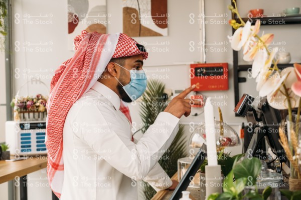 رجل بالزي السعودي يرتدي الكمامة في المقهى ويطلب كوب من القهوة