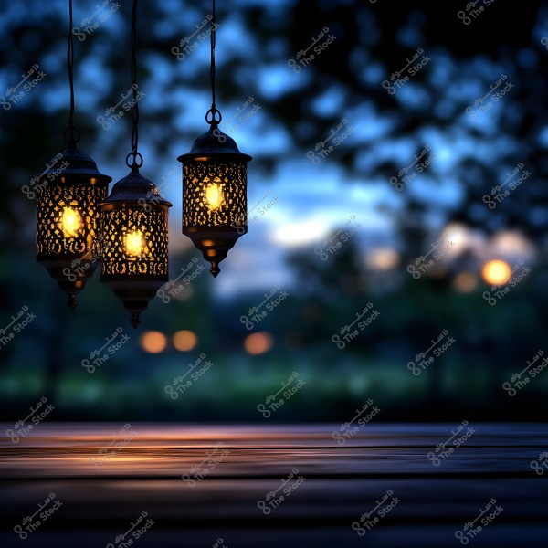 ثلاث فوانيس معدنية مزخرفة مضاءة معلقة أمام خلفية ضبابية لأشجار ومنظر طبيعي في المساء. الضوء المنبثق من الفوانيس يعطي إحساساً بالدفء والهدوء, مع انعكاسات خفيفة على السطح تحتها.