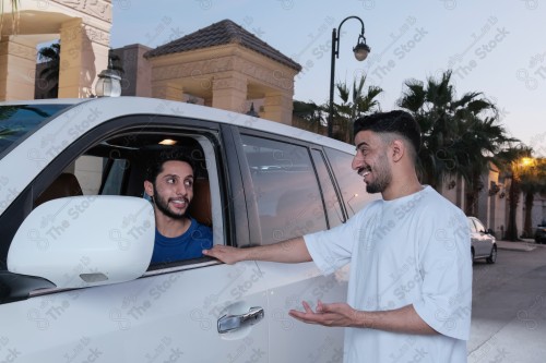 shot of two young Saudis chatting and having fun on the road, their features showing joy and happiness.