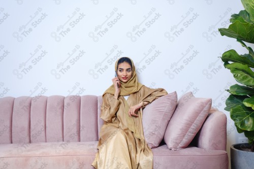 A Saudi girl sitting on the sofa and making different expressions using a mobile phone