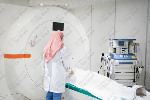 Saudi doctor wearing a medical uniform, working in the radiology department, helps the patient lie down in the MRI, health field, medical consultations and medical health services.