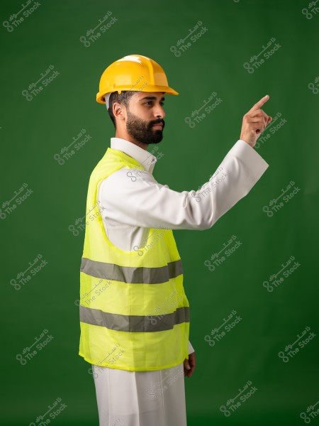 رجل يرتدي خوذة أمان صفراء وسترة عاكسة وقف أمام خلفية خضراء وهو يشير بإصبعه.