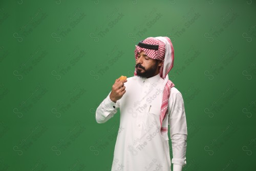 شاب سعودي على خلفية خضراء يرتدي الثوب و الشماغ، يقوم بعمل حركات بيده، يأكل الكعكة ، احتفالات العيد