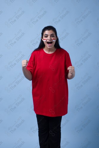 Portrait of a Saudi woman wearing a red T-shirt cheering the football team on a blue background and showing expressions of joy and enthusiasm, World Cup.