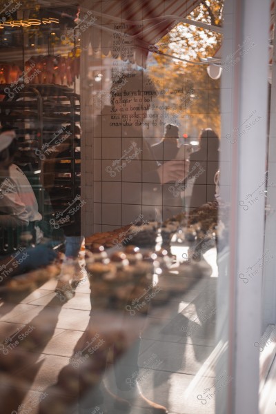 Reflection inside a bakery showing two people and several pastries on shelves, with a recipe written on the glass.