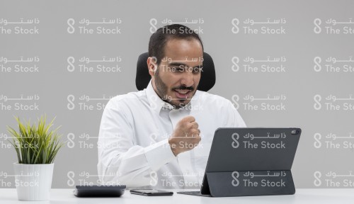 شاب سعودي يرتدي الثوب السعودي يعمل في مكتبه على الجهاز اللوحي