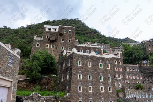 An ancient building built of stones in the middle of a group of windows surrounded by white paint while the sky looks cloudy during sunset, Rijal Almaa Heritage Village in the Asir region