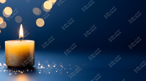 A lit golden candle with a soft flame stands on a dark blue surface, surrounded by circular bokeh light effects. The base of the candle is adorned with golden glitter that is also scattered on the surface around it. The background gives a sense of calmness and warmth.
