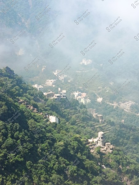 An image of a mountainous area covered with dense green vegetation and shrubs, featuring buildings and houses scattered along the mountain sides. Thick fog covers a significant portion of the scene, adding a mystical atmosphere. A winding road can be seen between the buildings scattered on the mountain terraces.
