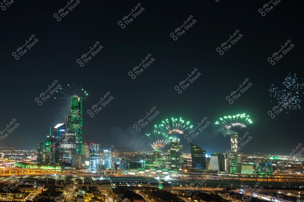 Image of Riyadh city skyline at night, featuring a cluster of illuminated skyscrapers with fireworks lighting up the sky in bright green colors. Roads and residential buildings are visible in the foreground, lit by the city\'s lights.