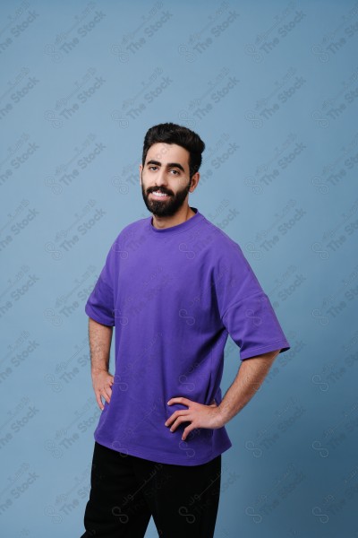 Portrait of a smiling Saudi youth, standing on a blue background.