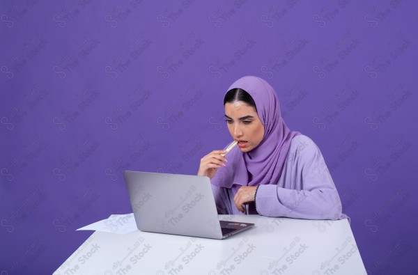 Portrait of a young Saudi woman wearing an abaya and hijab, holding a pen and thinking, against a purple background