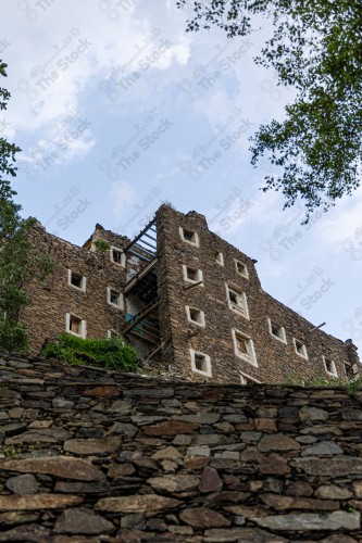 An ancient building built of stones with a group of windows surrounded by white paint during the day, Rijal Almaa heritage village in the Asir region