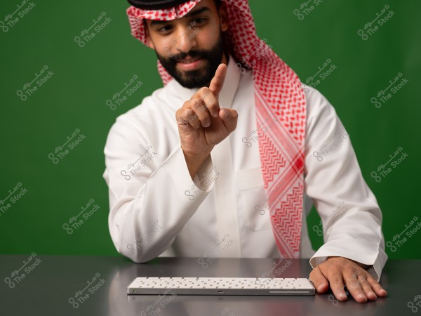 رجل يرتدي الزي التقليدي السعودي ويشير بإصبعه فوق طاولة توجد عليها لوحة مفاتيح.
