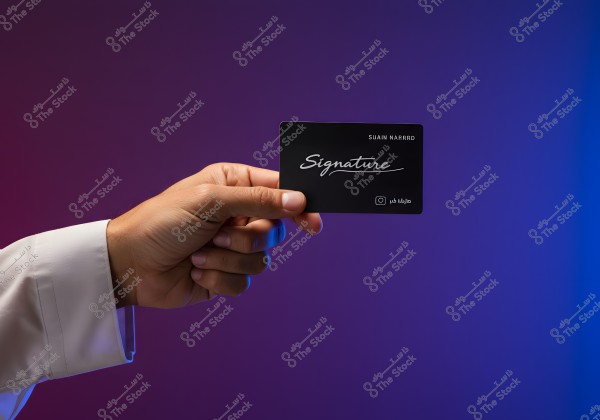 A hand wearing a white sleeve holds a black card with the word \"Signature\" written in elegant script. In the top right corner, the name \"SUAIN NARRRD\" is visible, and at the bottom, there is an Instagram icon with Arabic text. The background features a gradient of blue and purple colors.