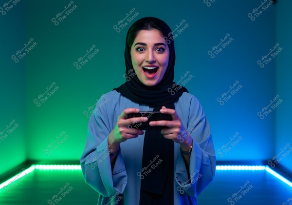 An image of a woman wearing a black abaya and hijab, looking excited while holding a video game controller. The background is lit with blue and green lights, creating a vibrant atmosphere.