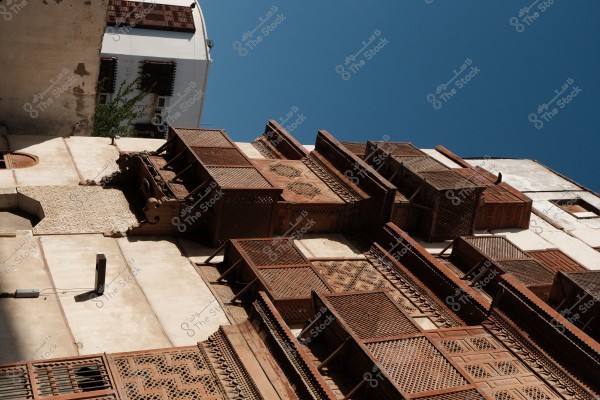 A view from below of an old building with wooden lattice windows featuring traditional designs, under a clear blue sky.