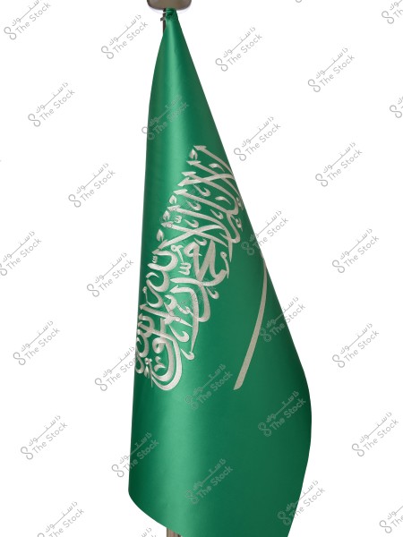 Image showing the flag of Saudi Arabia, featuring a green field with the shahada \"There is no god but God; Muhammad is the Messenger of God\" in white script above a horizontal sword. The flag is mounted on a simple pole.