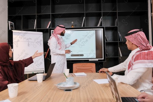 A Saudi man in traditional Saudi dress conducts a business meeting in the boardroom during the day