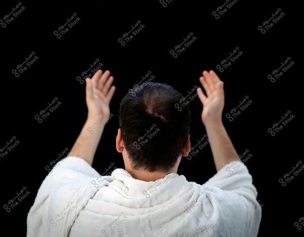 رجل يرتدي إحراماً ويرفع يديه للدعاء بخلفية سوداء.