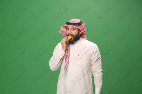 شاب سعودي على خلفية خضراء يرتدي الثوب و الشماغ، يقوم بعمل حركات بيده،يمسك الكعك و يأكله ، احتفالات العيد