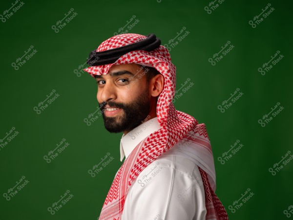 A man wearing traditional Arab attire with a red checkered shemagh stands in front of a green background.