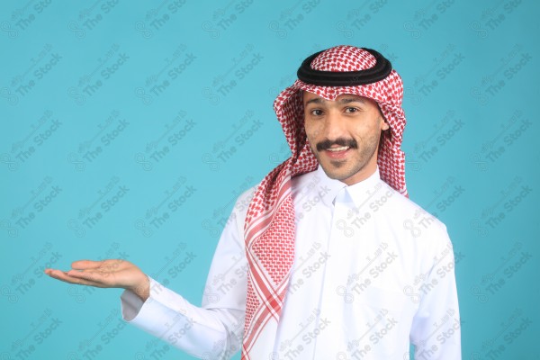 بورتريه رجل يرتدي الثوب ويقف أمام خلفية تركوازيه ، مبتسم ، يتفاعل بإشارات تعبيرية بيديه