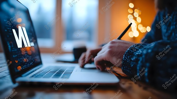 A person wearing a dark knitted sweater is working on a laptop in a dimly lit environment, possibly by candlelight or gentle lights. The laptop screen displays a distinctive modern logo. The background features blurred glowing lights, creating a warm and cozy atmosphere.