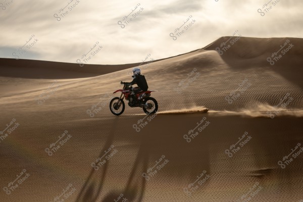 A motorcycle speeding across sand dunes in the desert. The golden sand glistens under a sky filled with light clouds, casting long shadows on the ground.