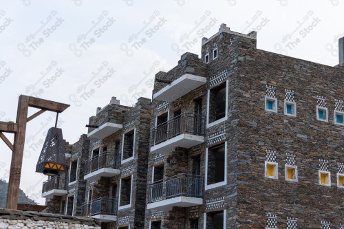 An ancient building built of stones in the middle of a group of windows surrounded by white paint while the sky looks cloudy during sunset, Rijal Almaa Heritage Village in the Asir region