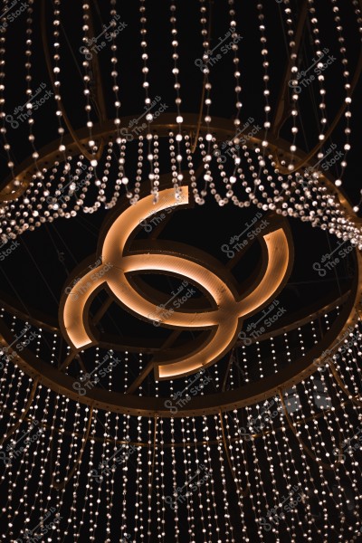 صورة لرمز مميز بشكل دائري مظلل بالأضواء الذهبية, معلق في سقف يحتوي على العديد من السلاسل الضوئية المتدلية بألوان دافئة, تضفي إحساساً بالفخامة والأناقة في أجواء مظلمة.

-