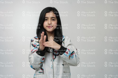 A smiling Saudi girl wearing a winter coat points with a sign language letter