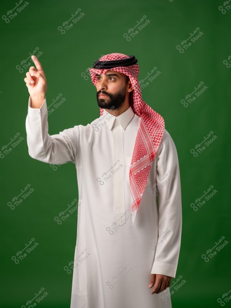 رجل يرتدي الزي الخليجي التقليدي يشير بإصبعه السبابة كما لو كان يتفاعل مع شاشة افتراضية أو يوضح نقطة معينة. الرجل يرتدي الثوب الأبيض والغترة باللونين الأحمر والأبيض مع العقال الأسود. الخلفية خضراء بسيطة.

-