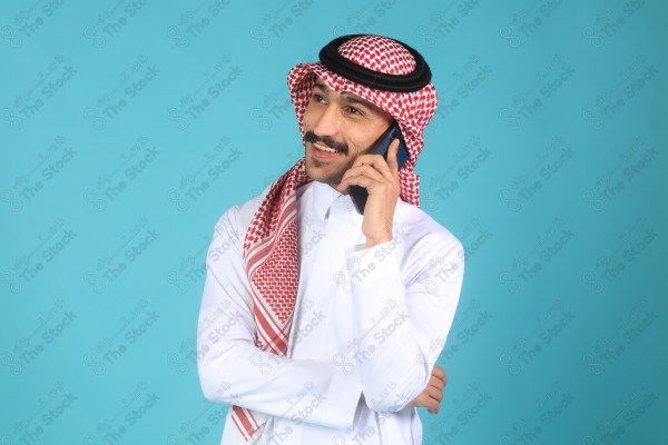 بورتريه رجل يرتدي الزي السعودي على خلفية تركواز، يتحدث بهاتفه وتبدوا على ملامحة السعادة، الاتصالات والتقنية