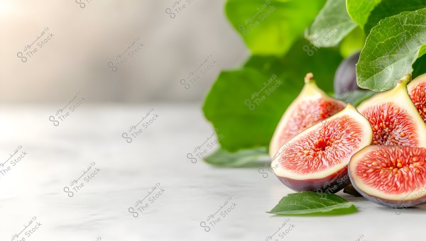 An image of fresh figs placed on a white surface. The figs are halved, revealing their rich red internal texture and small seeds. A backdrop of green fig leaves adds a natural touch to the scene.