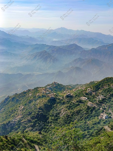 A scenic view of a green mountain with a ridge topped by scattered houses. The mountains recede dramatically into the distance, creating layers visible on the horizon. The clear sky adds a tranquil atmosphere to the scene.