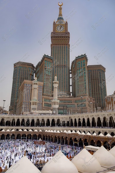 Image of the Makkah Royal Clock Tower next to the Grand Mosque, with crowds of people in the courtyard around the Kaaba.