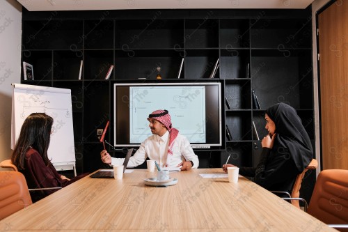 A Saudi man in traditional Saudi dress holds a meeting with Saudi female employees wearing abaya in the meeting room