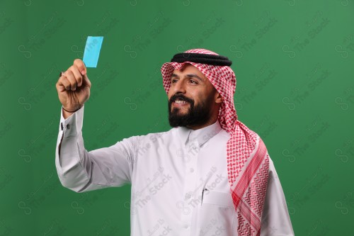 بورتريه رجل سعودي على خلفية خضراء مبتسم يحمل بطاقة الصرافة مستعد للتسوق