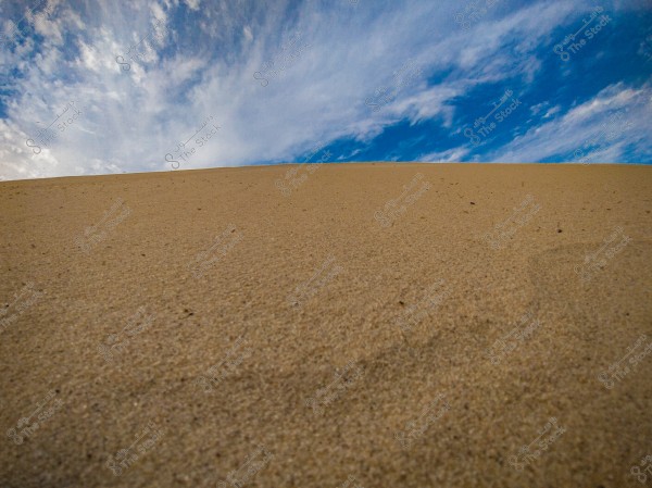 The image depicts a desert scene with a sand dune extending across the lower part of the image, under a wide blue sky. White clouds are scattered across the sky.