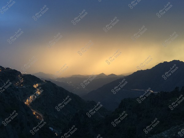 An image showing the view of Mount Soudah in Saudi Arabia during sunset. The winding road is lit through the mountains with street lights, and the horizon is filled with a beautiful blend of blue and orange hues. The sky appears cloudy, adding to the dramatic beauty of the scene.