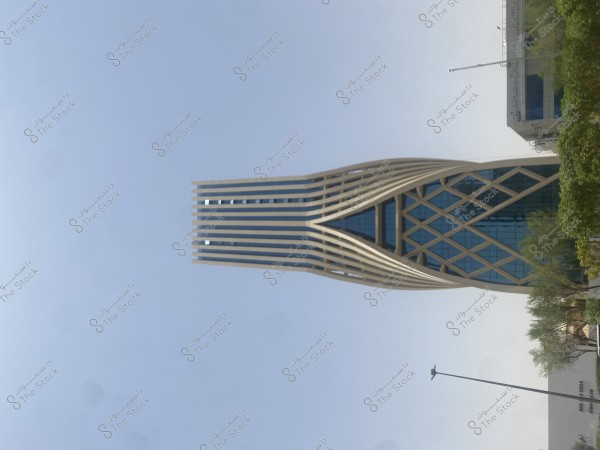 صورة لبرج معماري عصري يبرز بتصميمه المميز في مدينة حديثة. الجزء السفلي من البرج مكون من هيكل قطري يشبه الشبكة, يتضمن إطارًا من الخطوط البيضاء المستقيمة تلتقي لتشكل نمطًا ماسيًا. الجزء العلوي من البرج يتميز بخطوط رأسية ممتدة. تظهر حديقة صغيرة بأشجار أمام المبنى.