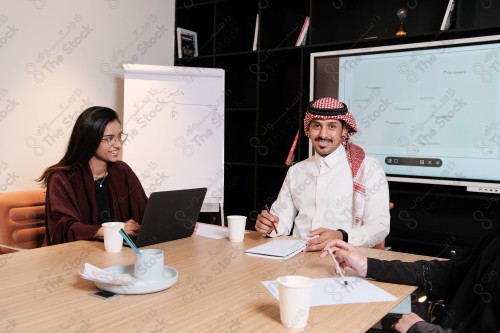 A Saudi man in traditional Saudi dress holds a meeting with Saudi female employees wearing abaya in the meeting room