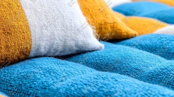 A close-up image of colorful cushions made from a coarse fabric. The cushions are arranged to show the texture of the fabric, with the front cushion in blue, accompanied by a white cushion, and two yellow cushions in the background. The fabric texture is prominently displayed, highlighting its coarse weave.