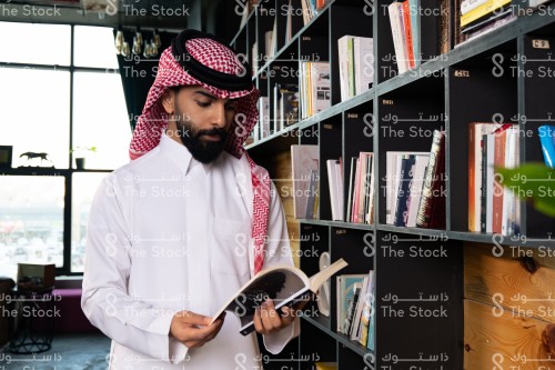 رجل سعودي يرتدي الزي السعودي التقليدي يتصفح أحد الكتب في المكتبة